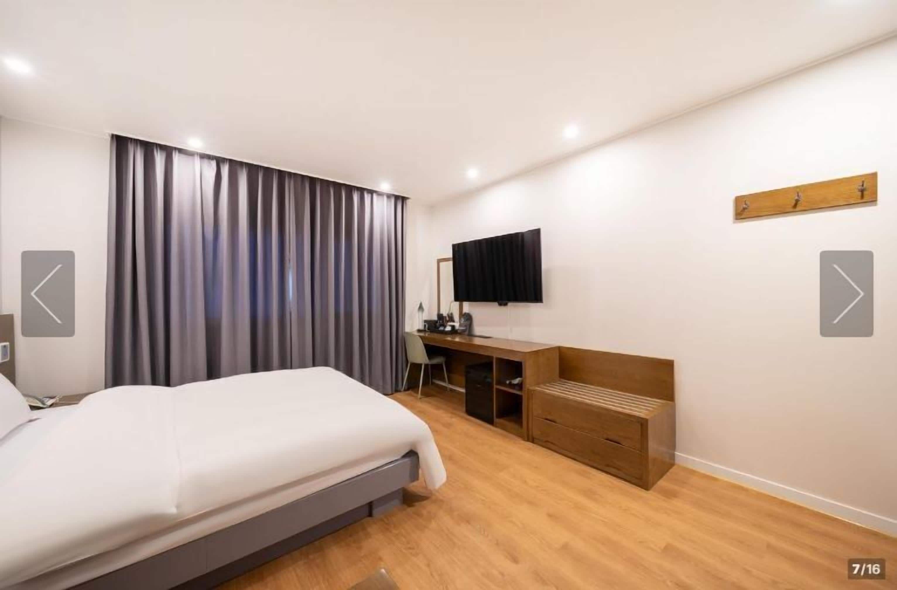A modern hotel room with a large bed, a desk, a chair, and a flat-screen TV mounted on the wall.