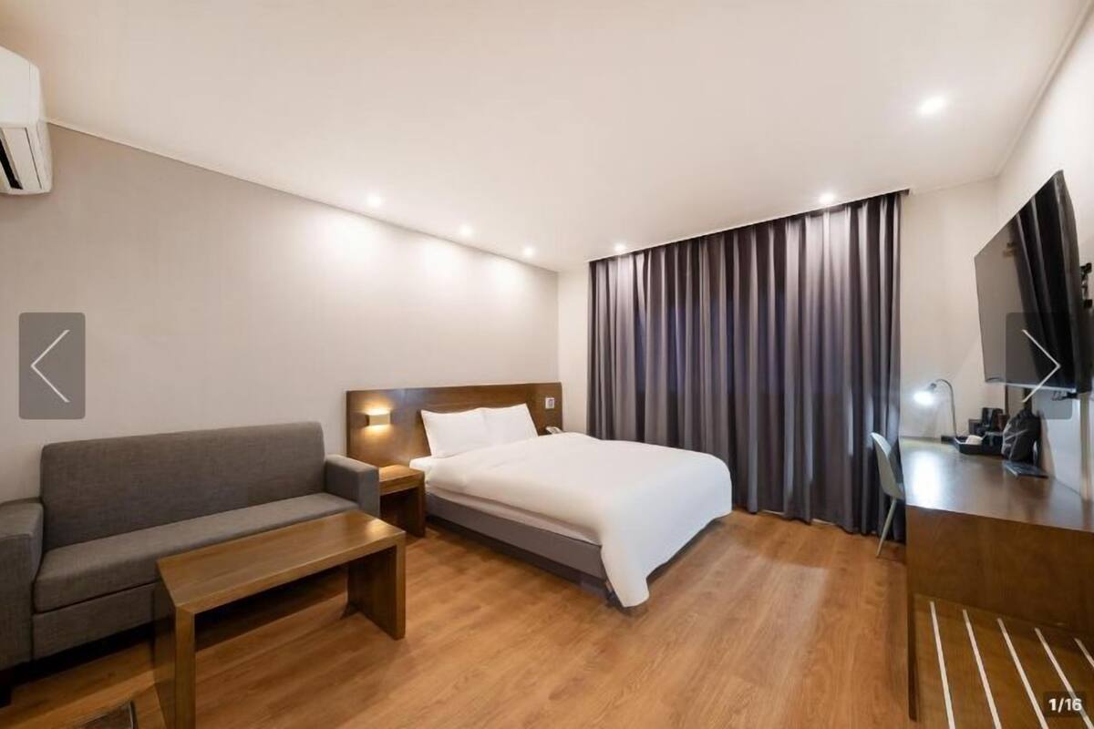 Una habitación de hotel moderna con una cama, un sofá, una mesa de centro de madera, un escritorio y un televisor.