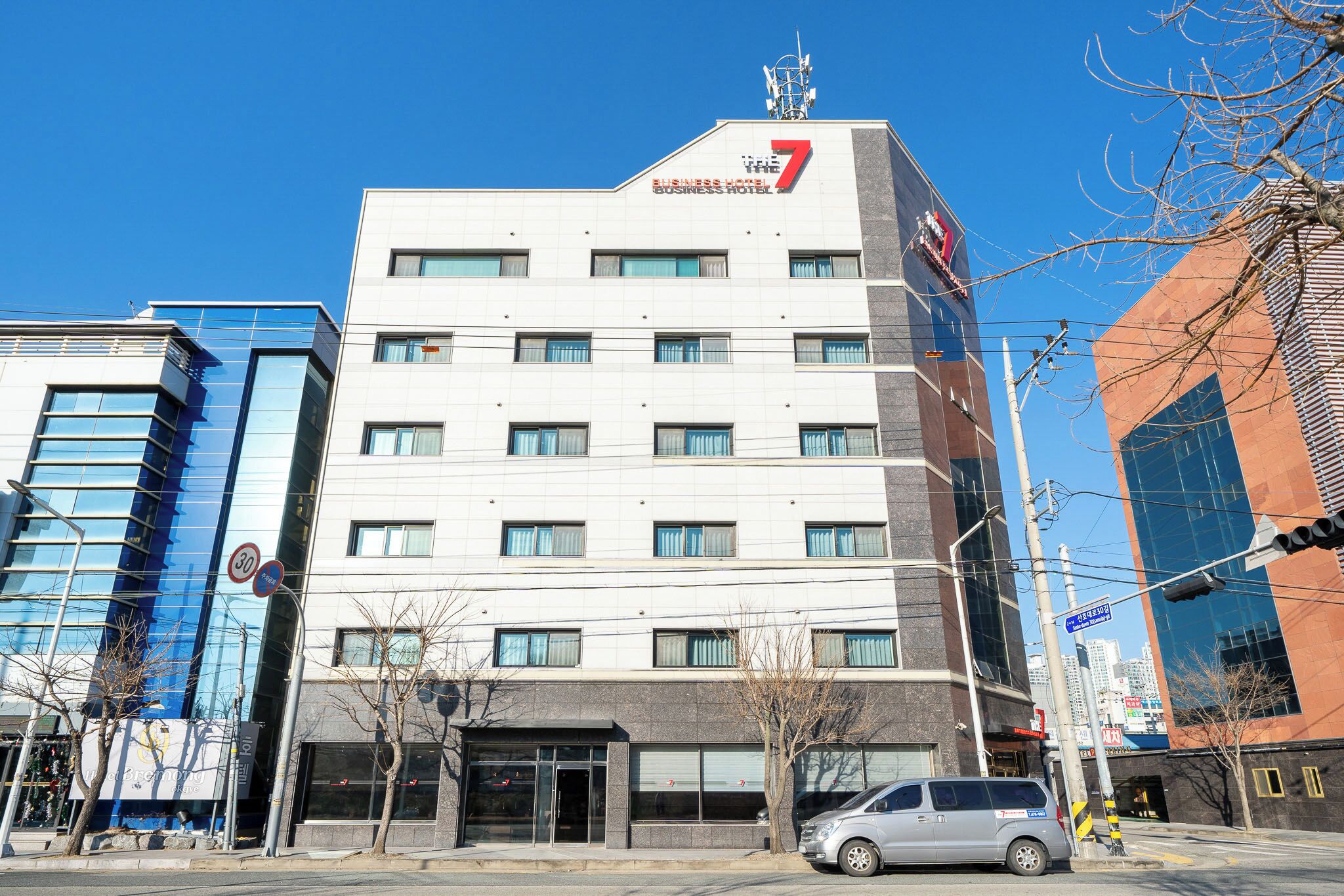 Un hôtel à plusieurs étages au design moderne, caractérisé par un grand logo en forme de « 7 » sur la façade, de grandes fenêtres et un toit plat.