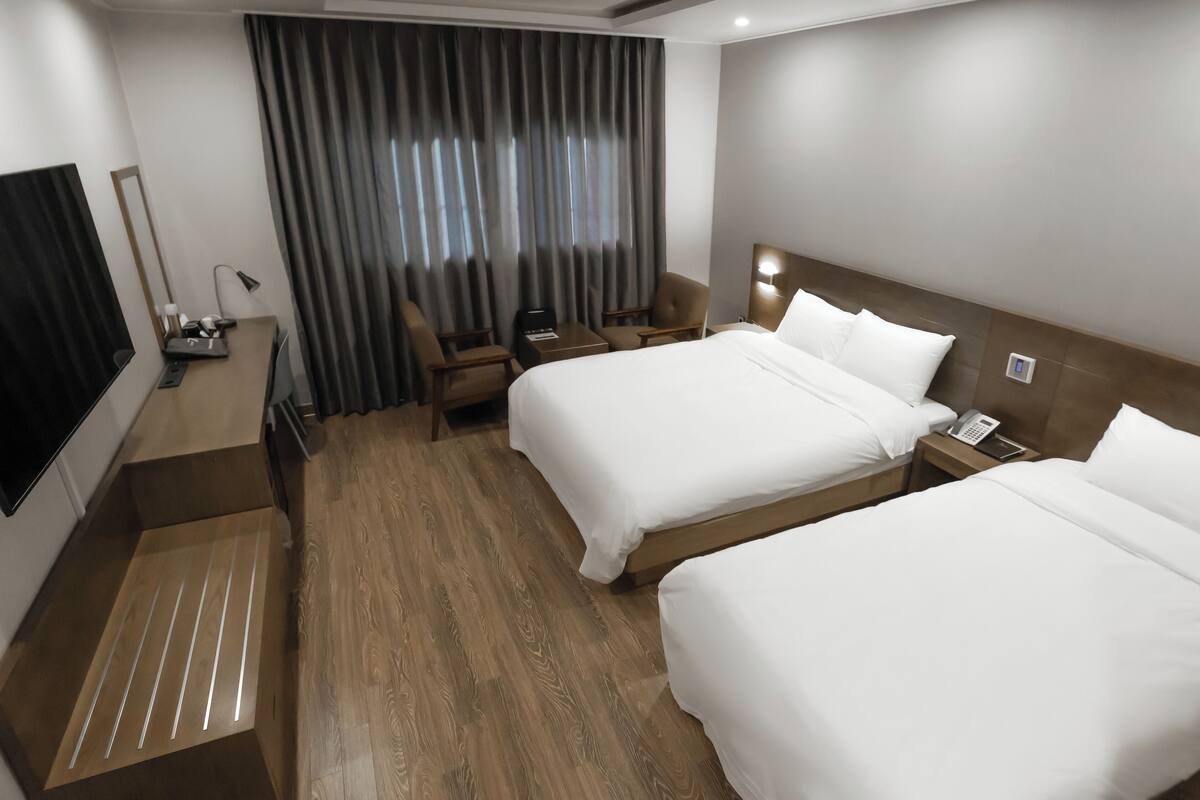 Una habitación de hotel con dos camas, un escritorio, una silla, un televisor y una cortina.