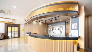 Un espace d’accueil doté d’un comptoir de réception en bois aux lignes courbes, d’une carte du monde affichée au mur et d’un panneau indiquant « Accueil/Renseignements ».