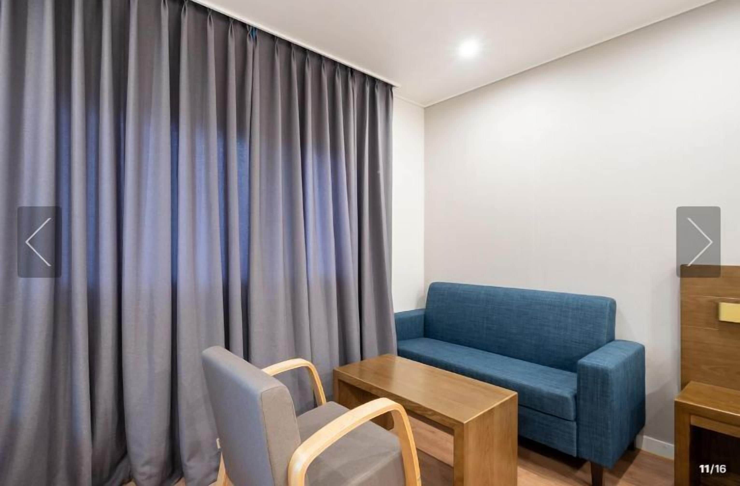A room with a blue sofa, a wooden coffee table, and grey curtains.