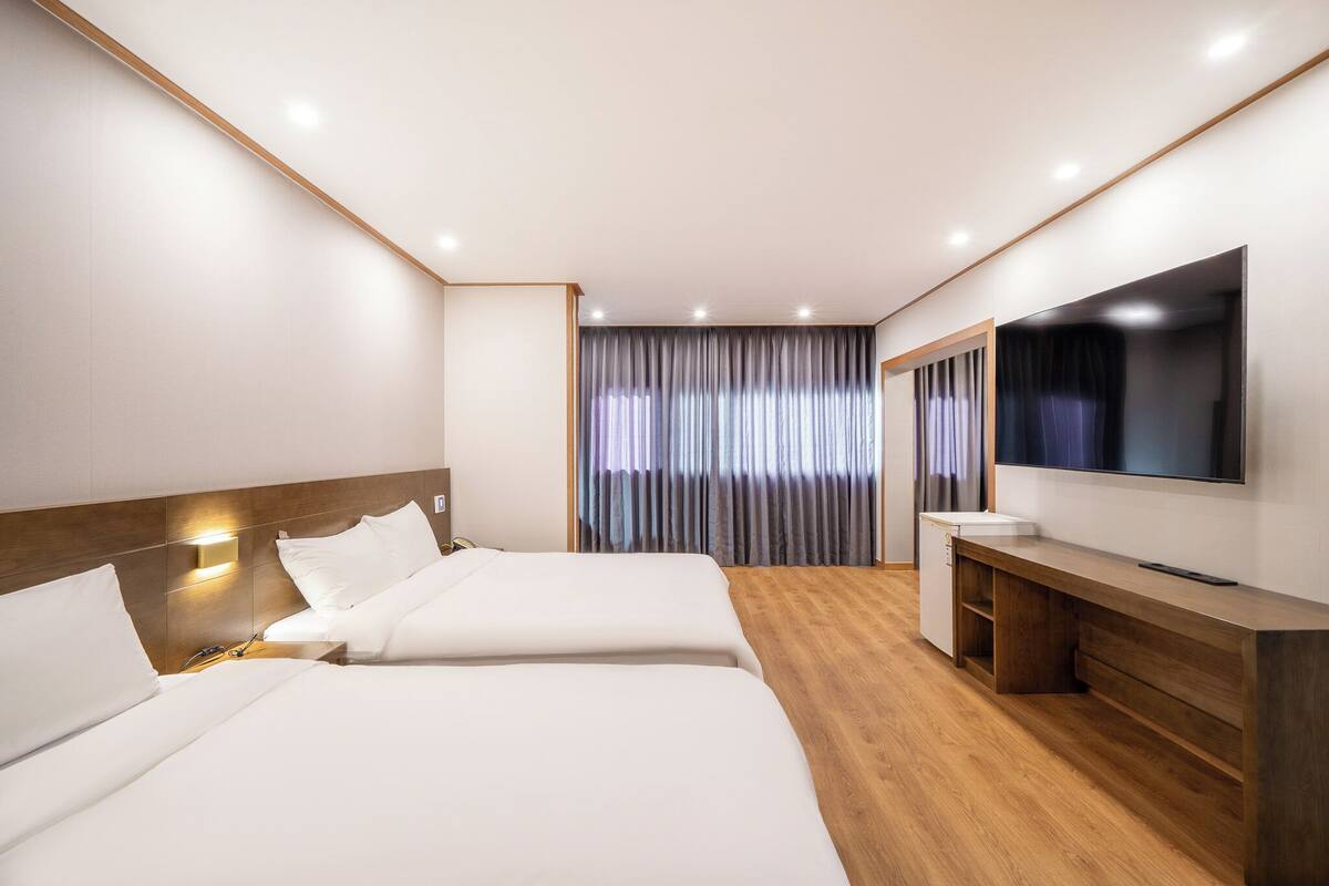 Una habitación de hotel con dos camas, televisión, escritorio y ventana con cortinas.