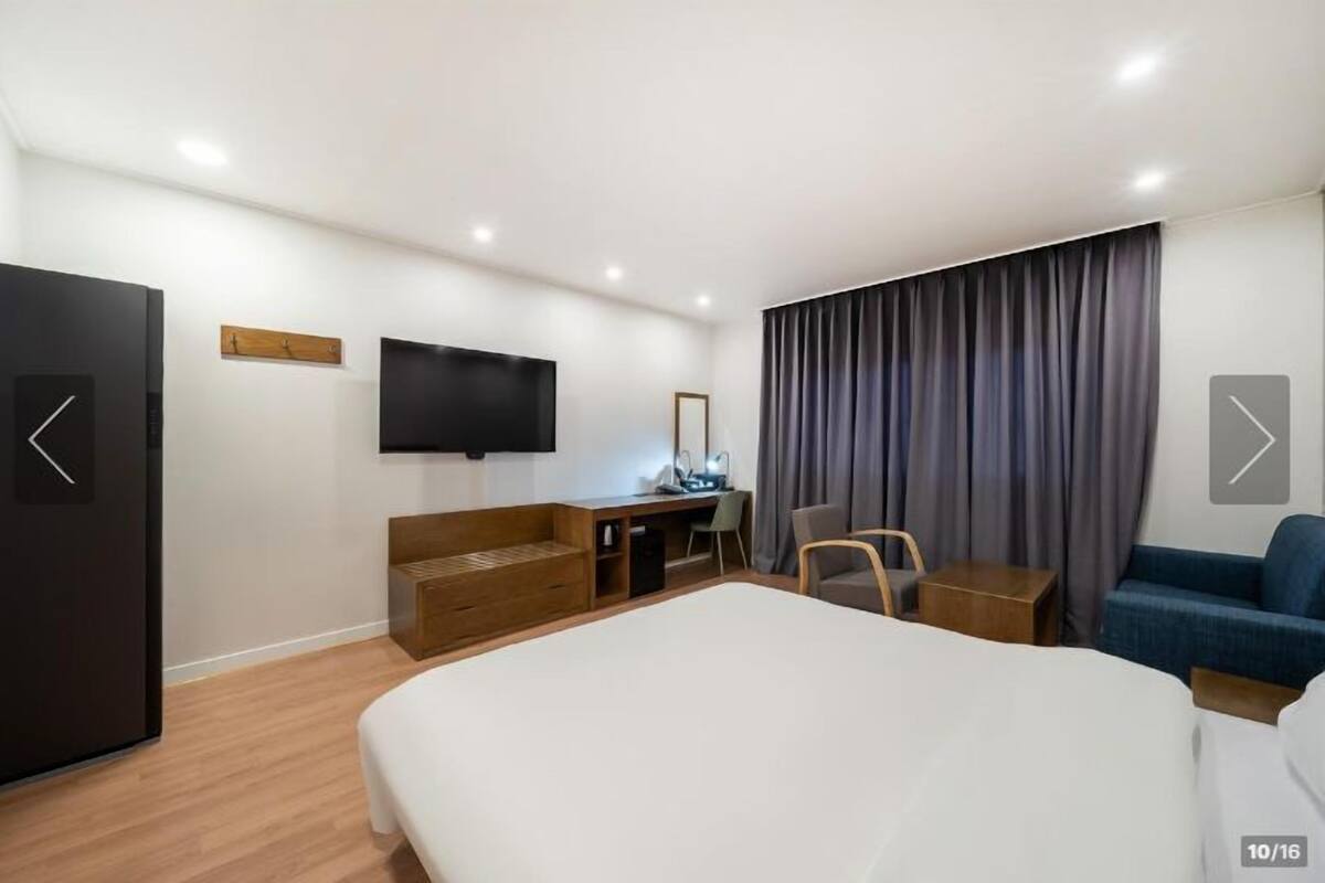 Una habitación de hotel moderna con una cama grande, un escritorio con una silla, un televisor montado en la pared y un armario.