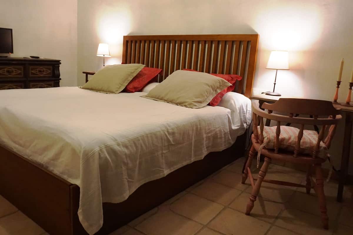 Un lit double avec une tête de lit en bois, deux lampes de chevet et une chaise à ossature en bois.