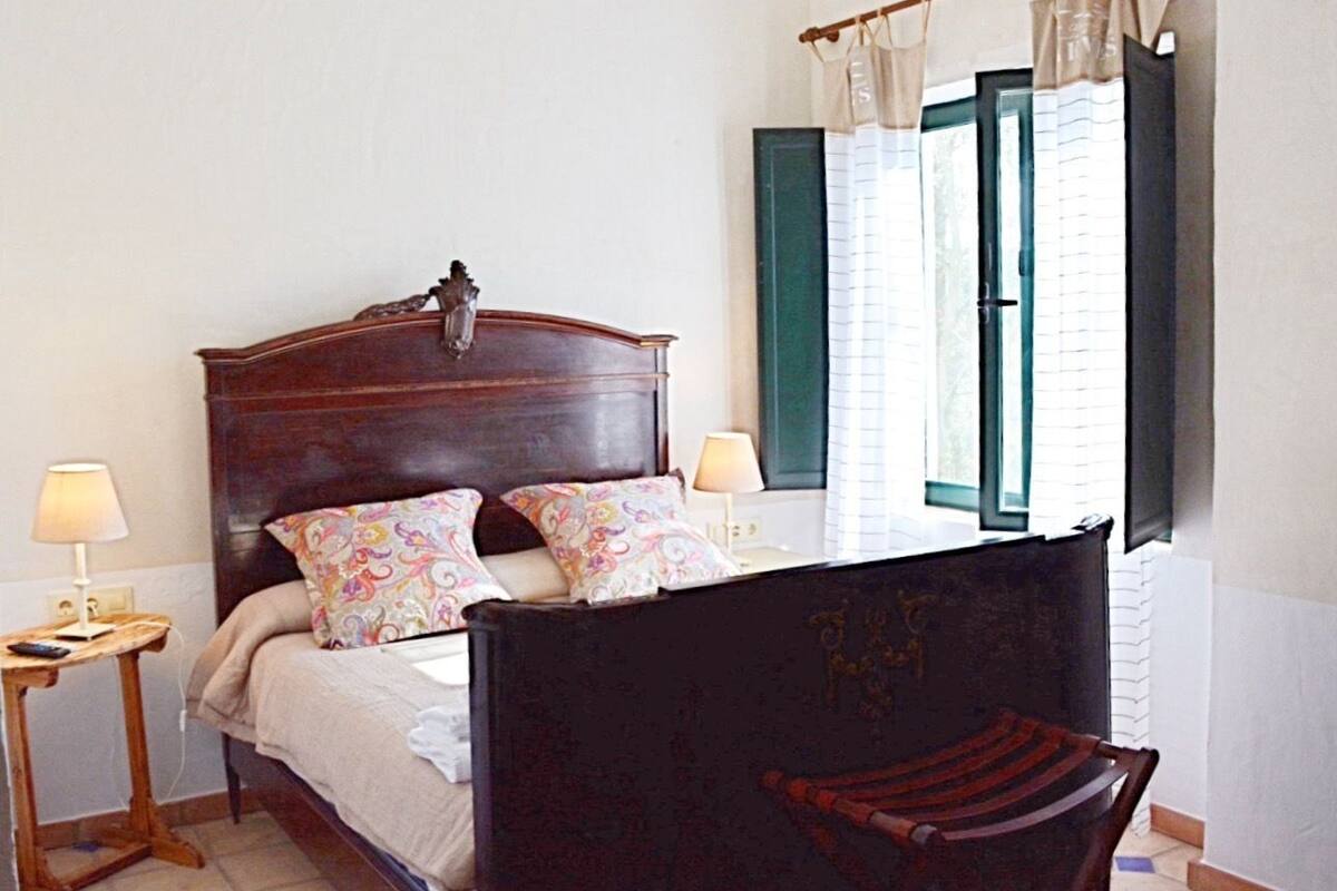 Une chambre à coucher avec un lit en bois, deux lampes de chevet, une chaise et une fenêtre avec des rideaux.