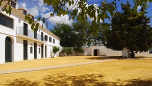 Une cour avec un bâtiment blanc, des arbres et un ciel dégagé.