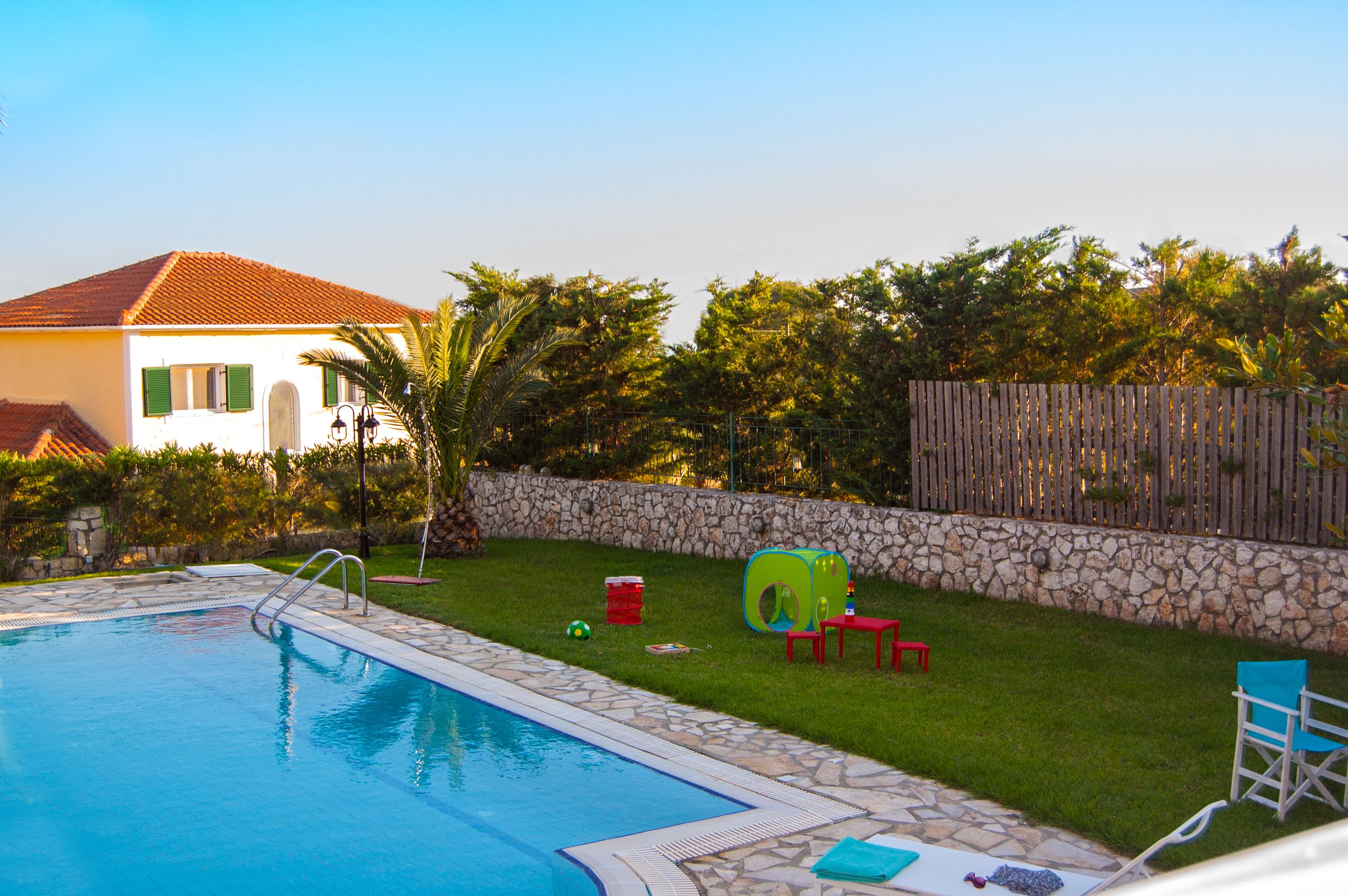 A swimming pool with a stone border, a stone wall, and a wooden fence.