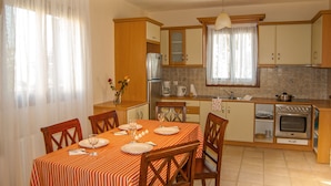 A compact kitchen with wooden cabinets, a built-in oven, and a dining area with a striped tablecloth.