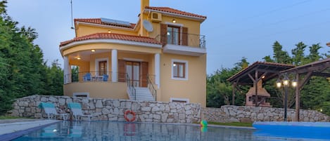 A two-story house with a swimming pool, stone wall, and a covered patio area.