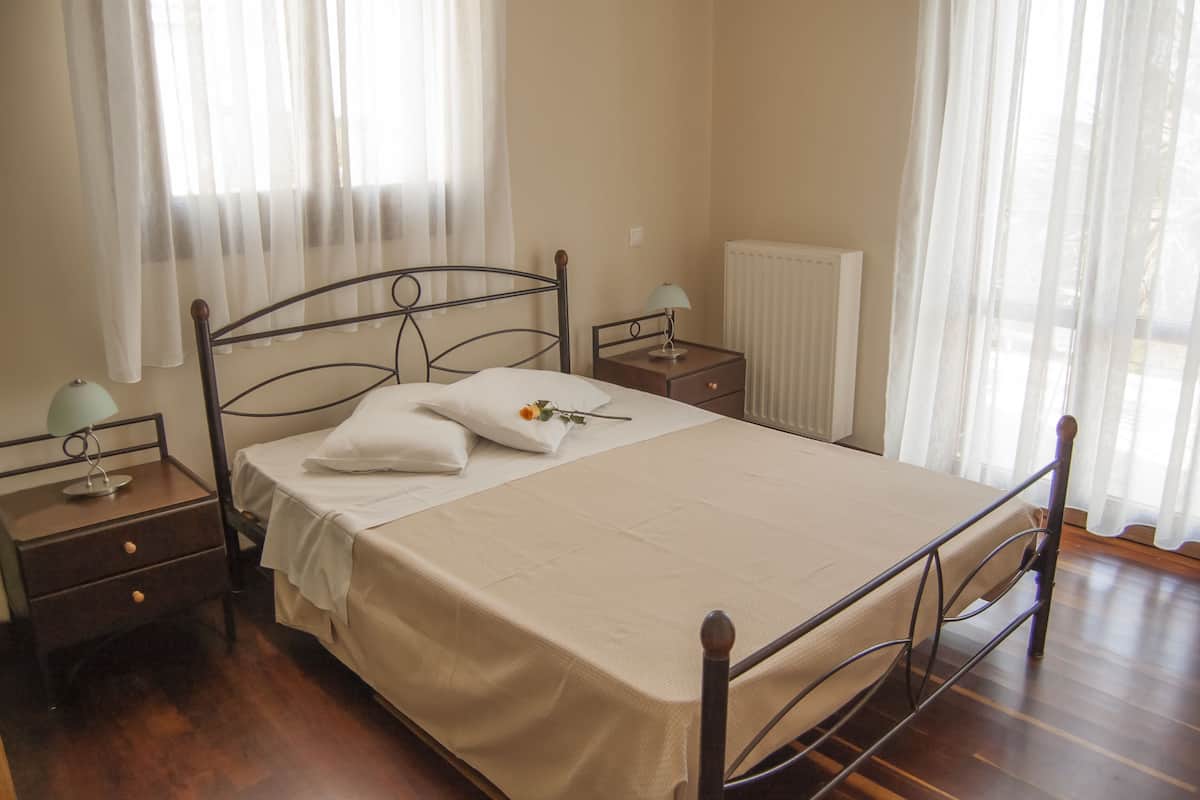 A neatly made bed with a white bedspread, two bedside tables with lamps, and a radiator in the background.