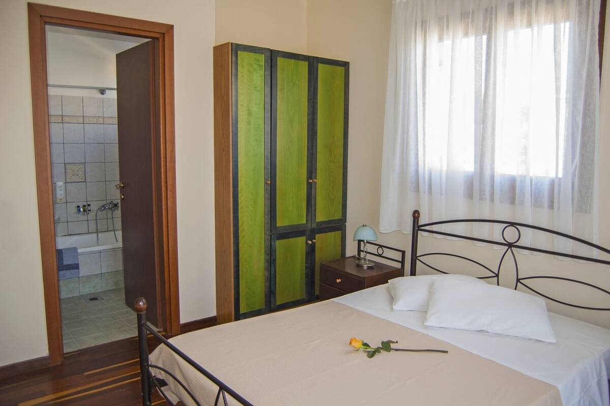 A bedroom with a bed, a nightstand, a wardrobe, and a bathroom visible through an open door.
