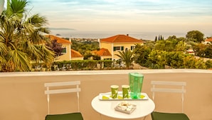 A balcony with two chairs and a table, overlooking a residential area with houses and greenery.