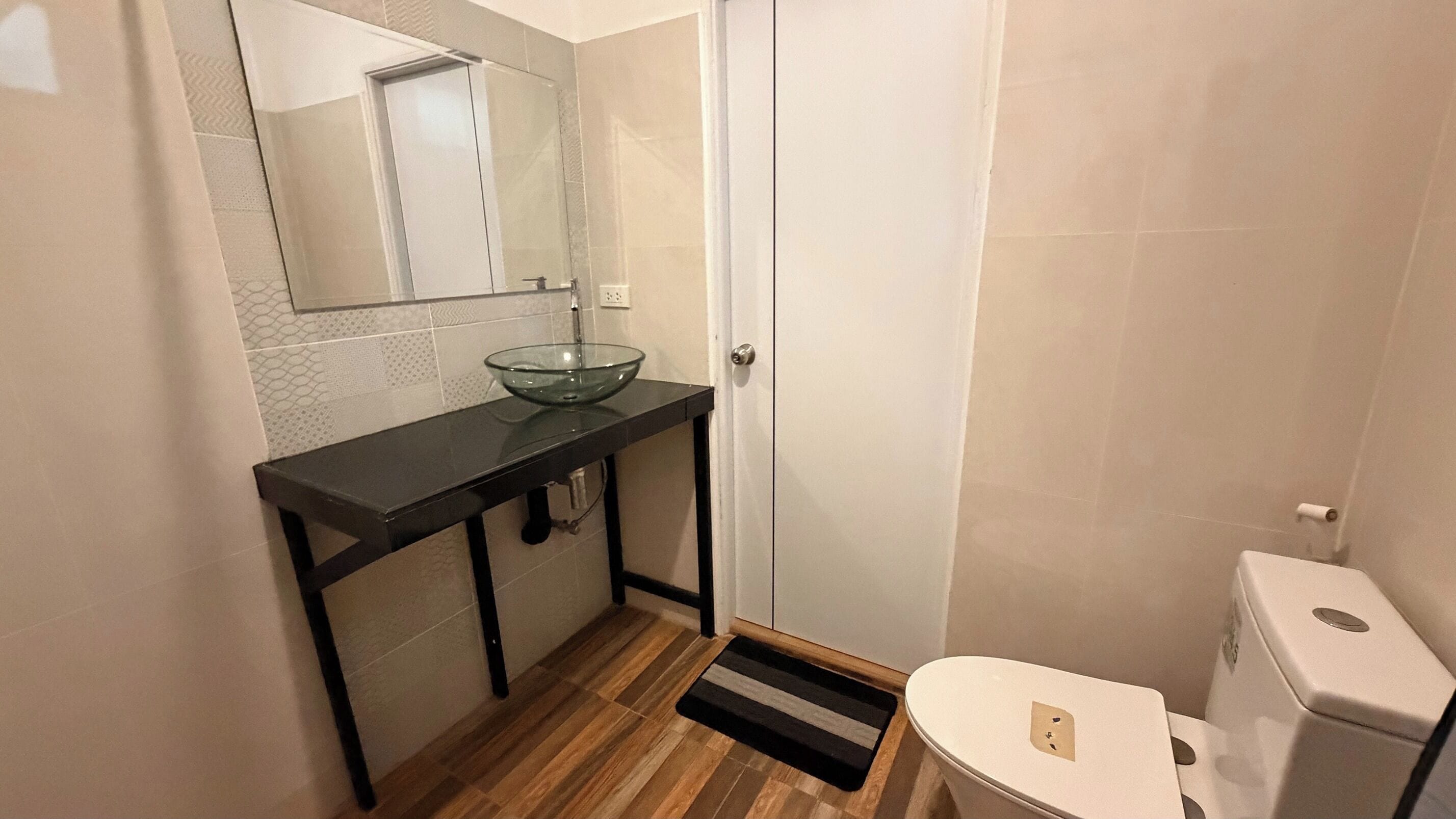 Une salle de bain avec un lavabo en verre, des toilettes et un plancher en bois.