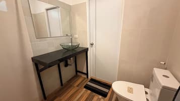 Une salle de bain avec un lavabo en verre, des toilettes et un plancher en bois.