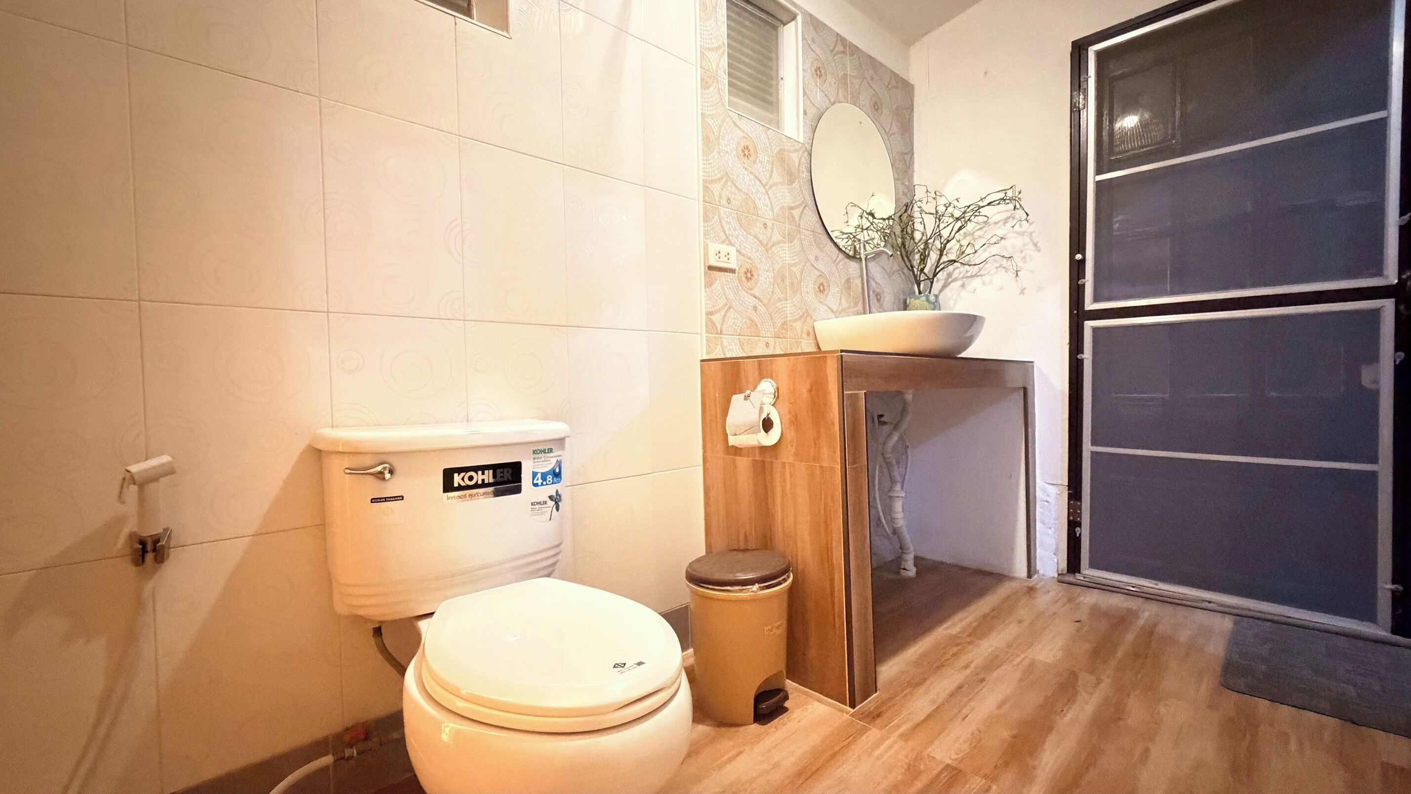 A modern bathroom with a toilet, a trash bin, a sink with a mirror, and a wooden cabinet.