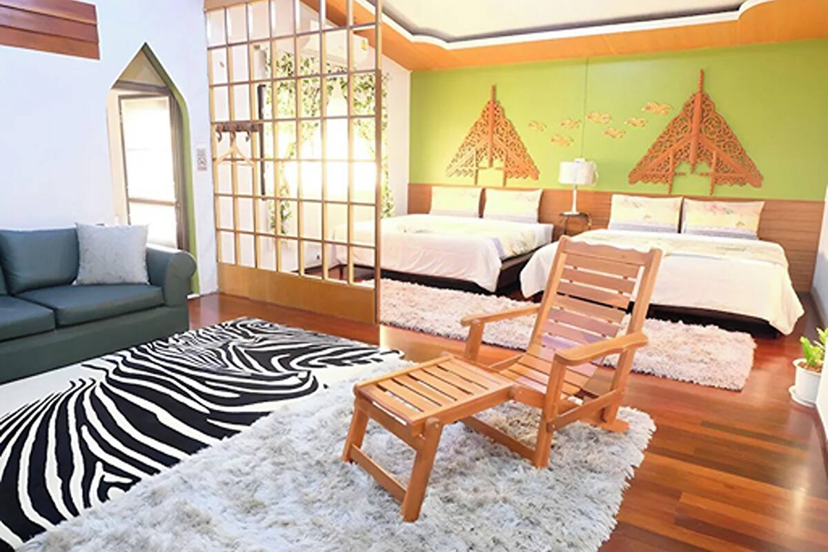 Una habitación con una cama, una silla de madera, un alfombra de zebra, una pared verde y una ventana con vistas.