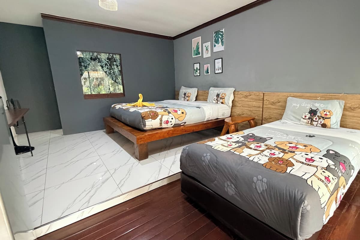Un dormitorio con dos camas, un cabecero de madera, un ventanal pequeño y una pared con cuadros.