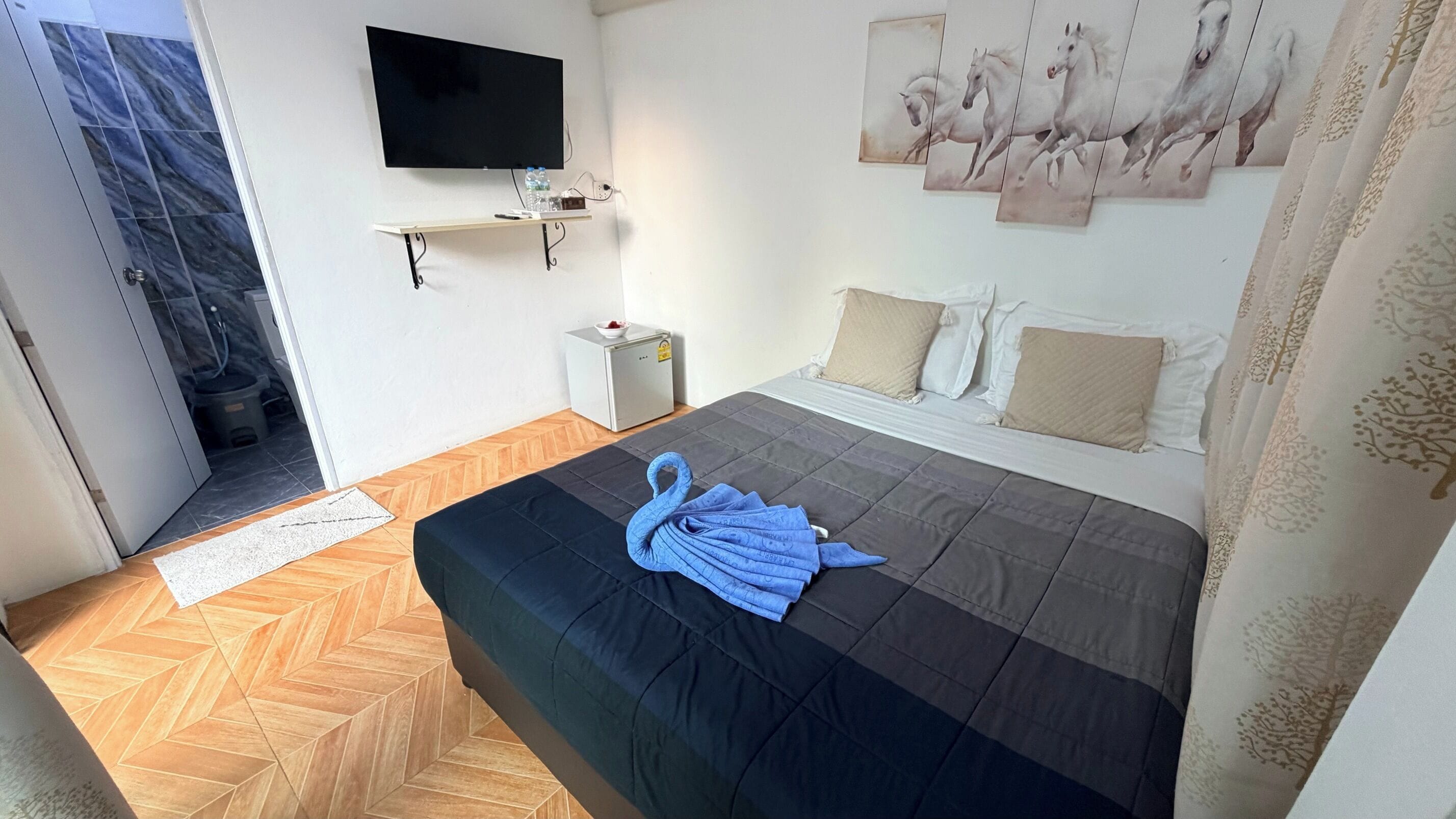 Habitación de hotel con cama, televisión, escritorio pequeño, silla, ventana y puerta.