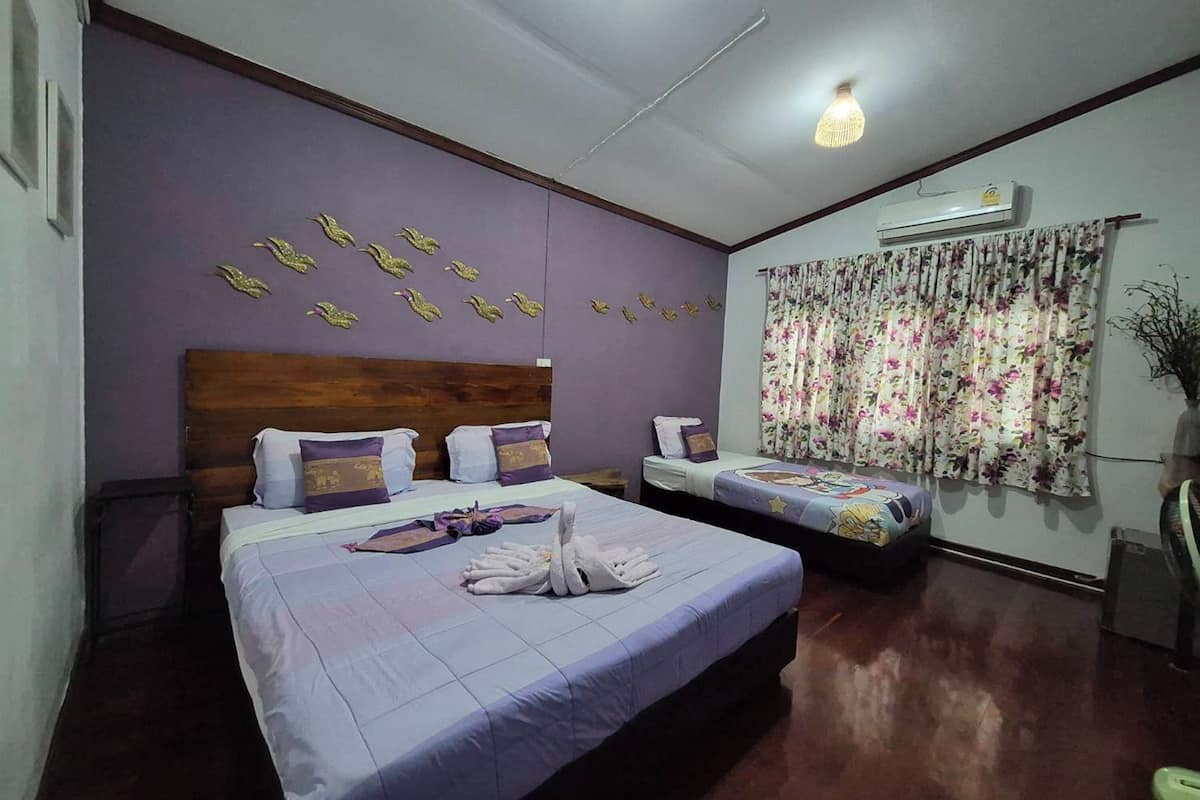 Habitación de hotel con dos camas, cabecera de madera, cortina estampada con motivos florales y un equipo de aire acondicionado.