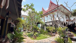 Un patio con plantas en macetas, un pequeño estanque y un edificio tradicional con techo rojo.