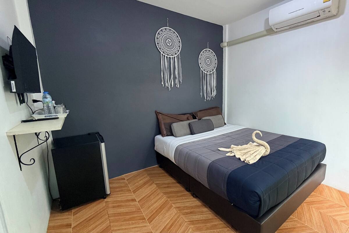 Un dormitorio con una cama, obras de arte en la pared, un escritorio con una computadora y un aire acondicionado.