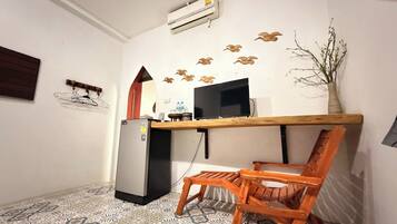 A compact room with a kitchenette, a wooden chair, a TV, and decorative wall art.