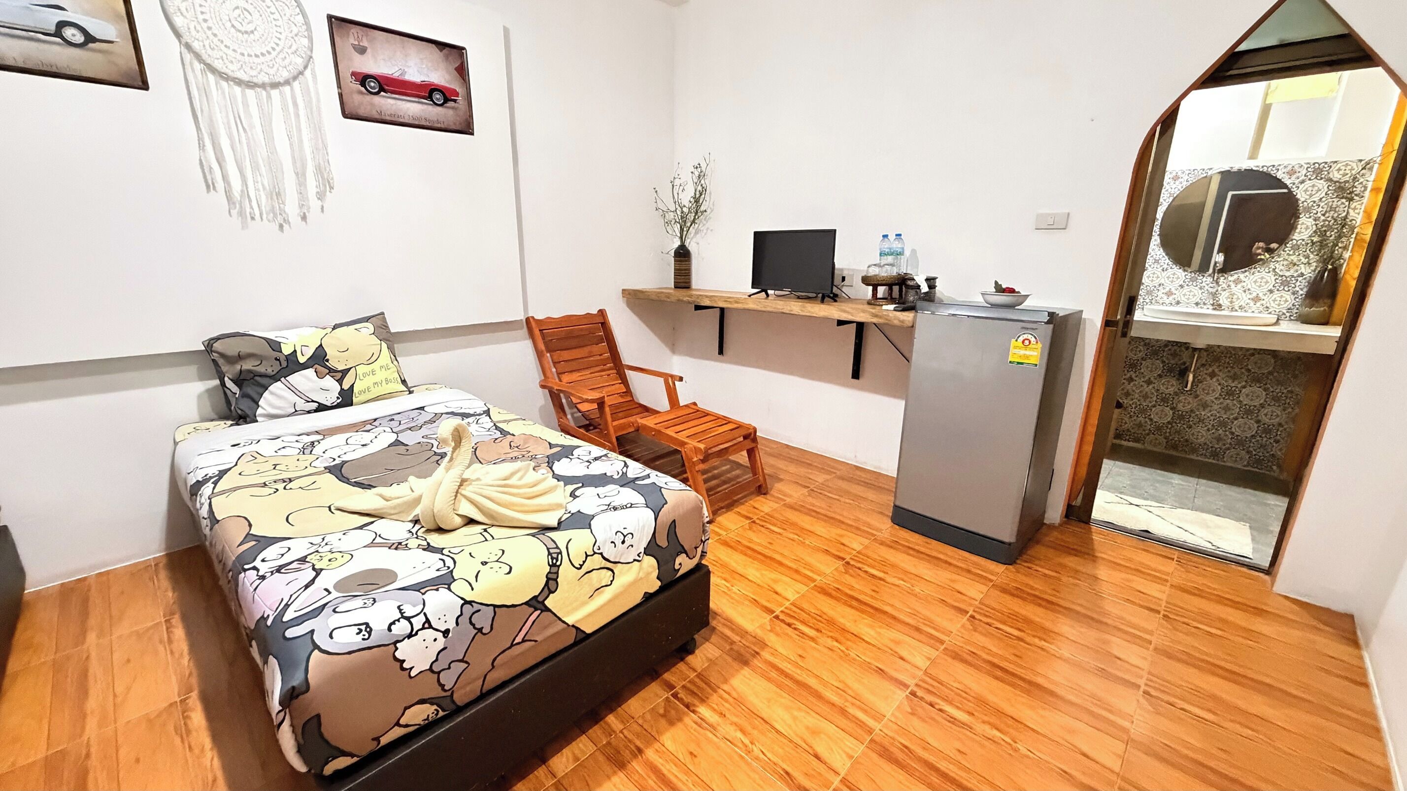 A bedroom with a bed, a desk, a chair, a refrigerator, and a decorative wall piece.
