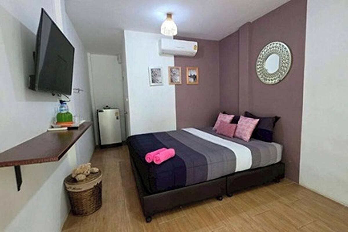 Un dormitorio con cama, televisión, refrigerador pequeño y aire acondicionado instalado en la pared.