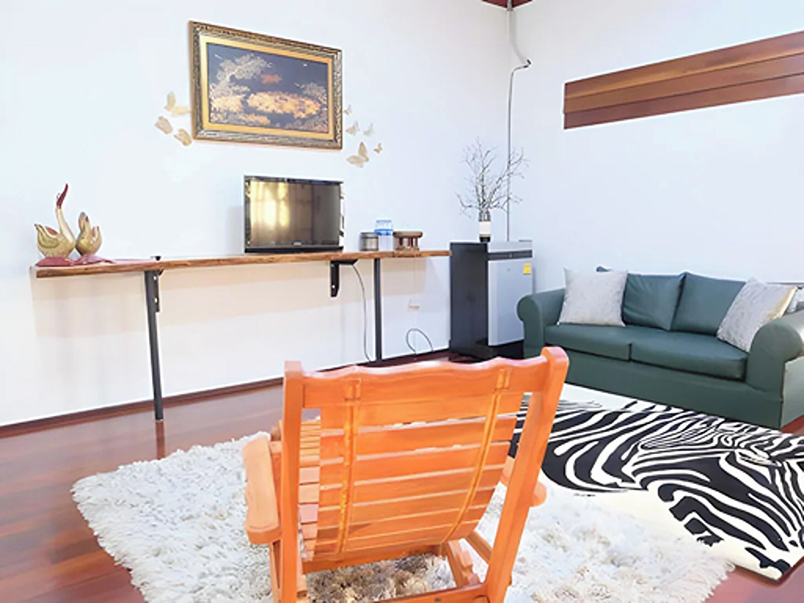 A living room with a wooden chair, a sofa, a zebra-patterned rug, a framed picture on the wall, and a small table with decorative items.