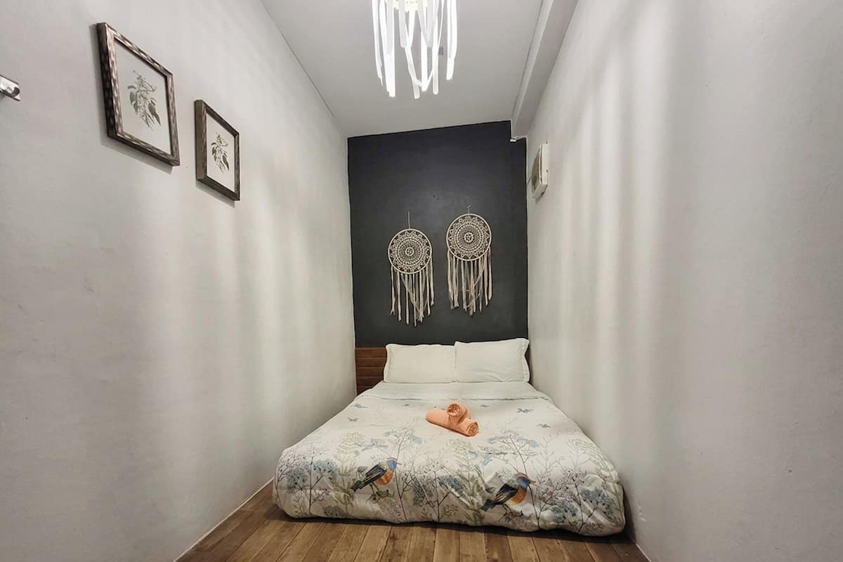 Un dormitorio con cama, suelo de madera, pared oscura y dos atrapasueños colgados.