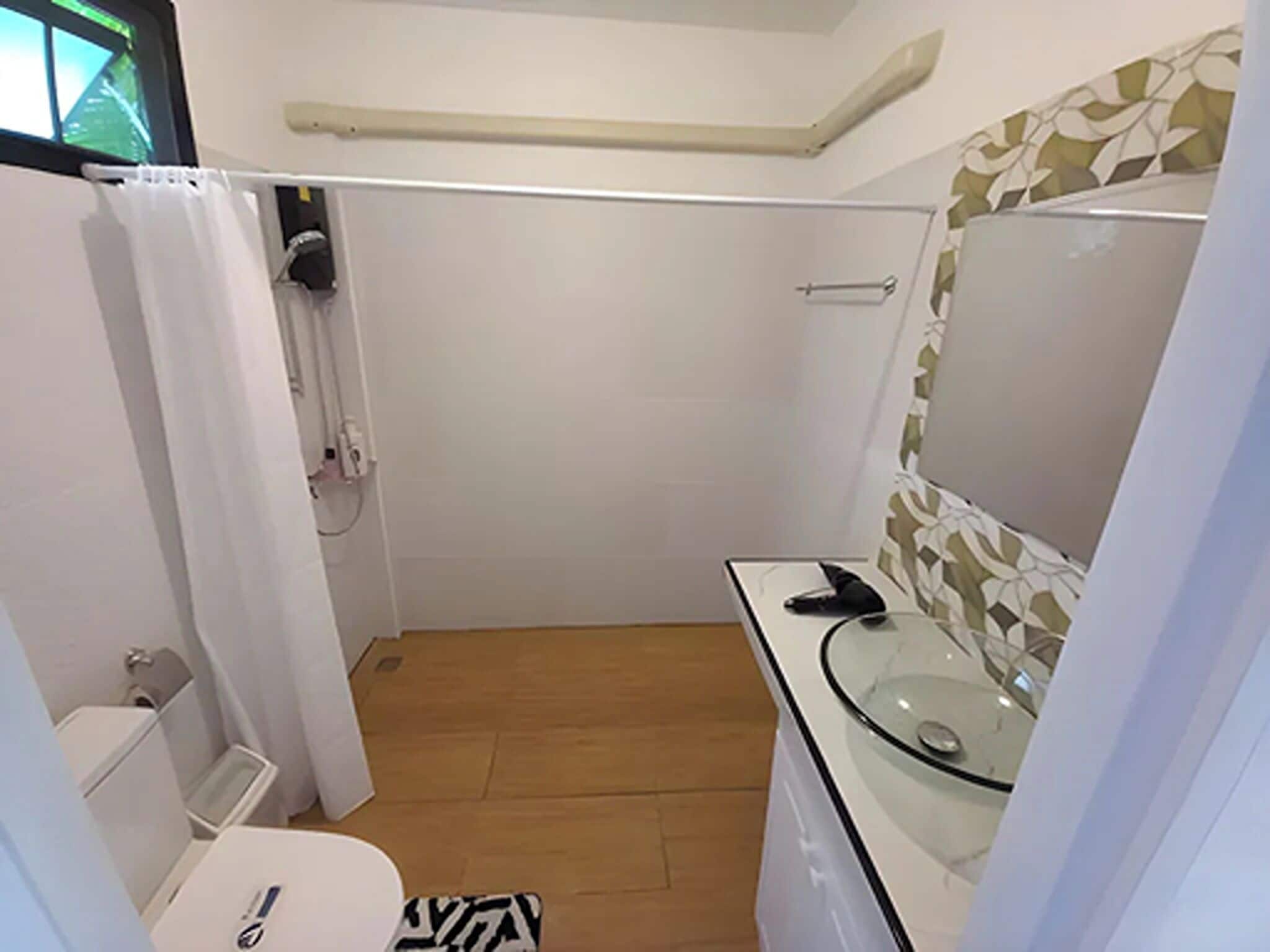 A small bathroom with a toilet, a glass sink, a mirror, and a shower area.
