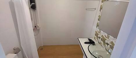 A small bathroom with a toilet, a glass sink, a mirror, and a shower area.