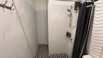 A shower with a handheld showerhead, a handheld showerhead, and a shower caddy with toiletries.