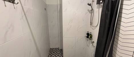 A shower with a handheld showerhead, a handheld showerhead, and a shower caddy with toiletries.