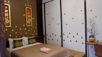 A hotel room with a bed, pillows, a bedside table with a vase, and a wall with decorative leaf decals.