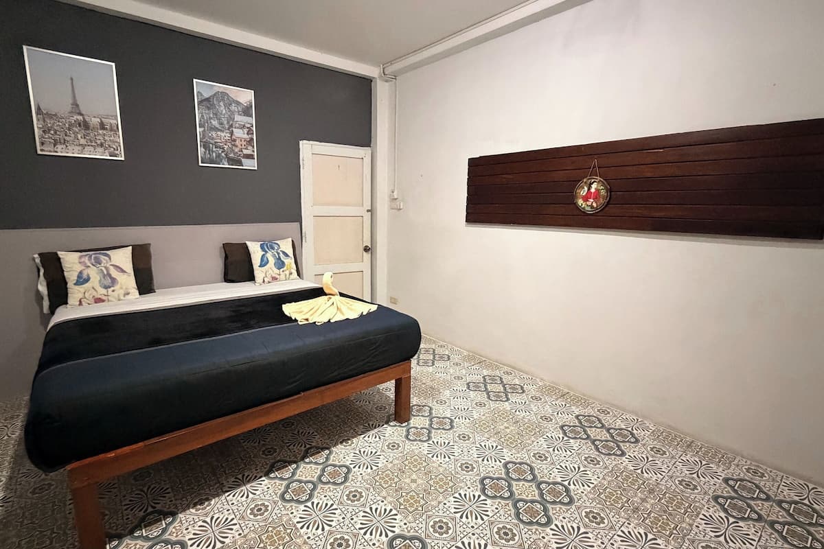 Un dormitorio con cama, un banco, baldosas de suelo estampadas, una puerta y dos cuadros en la pared.