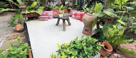 Un jardín con una mesa de piedra, taburetes de madera y varias plantas en macetas.