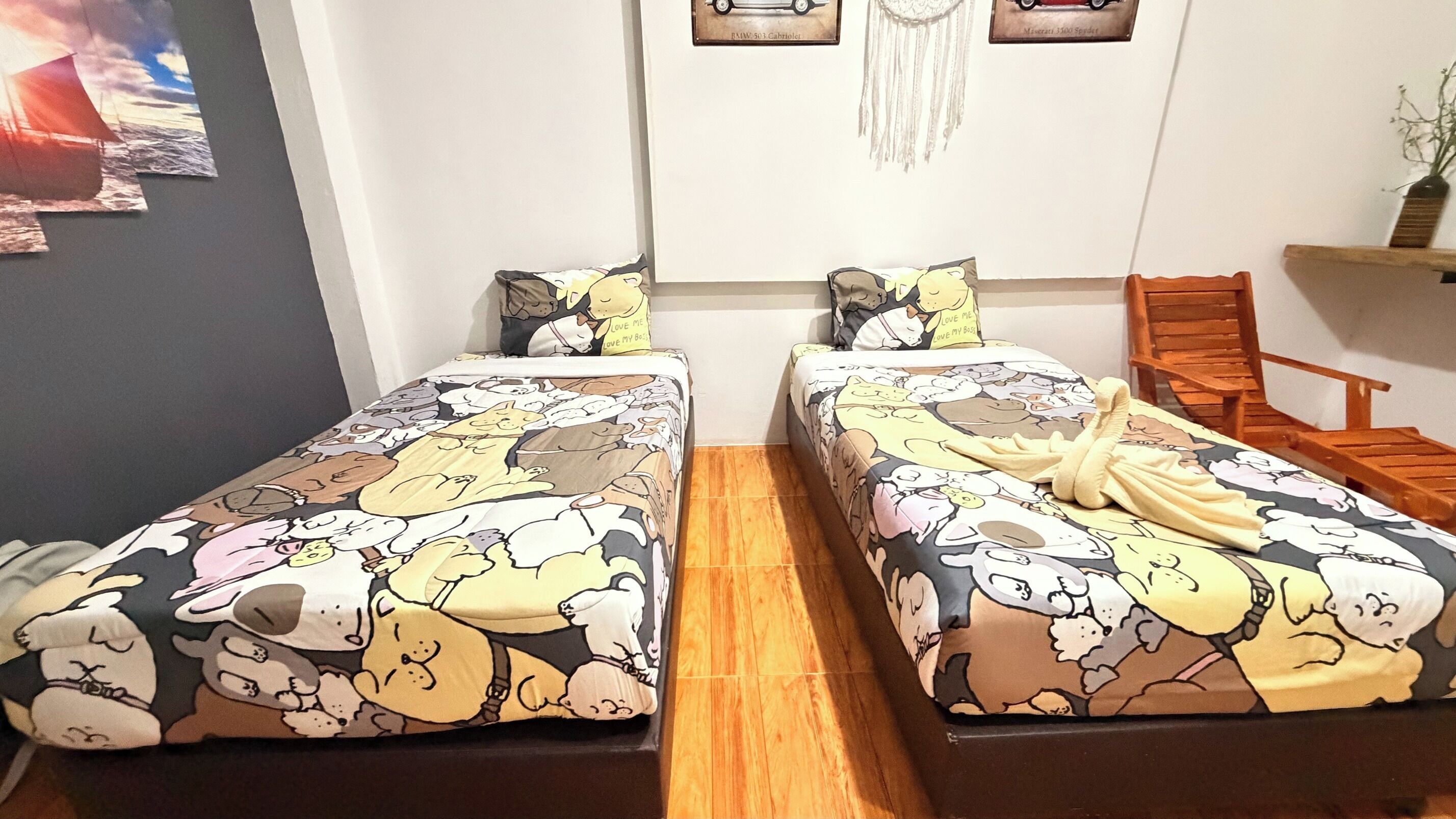 Un dormitorio con dos camas, cada una con una colcha de estampado de animales de caricatura, una silla de madera y un estante en la pared con una planta.