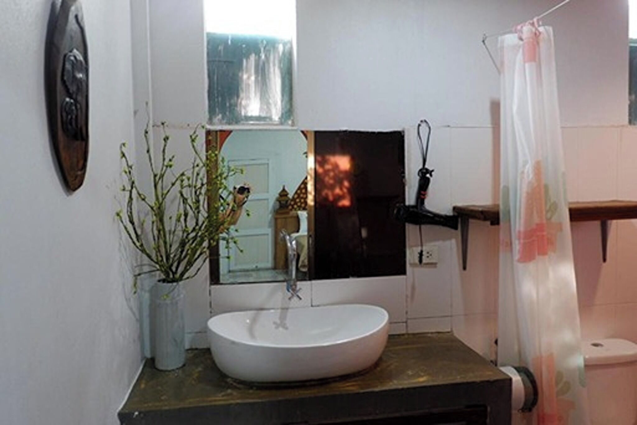 Une salle de bain avec un lavabo blanc, un miroir, une plante en pot et un rideau de douche.