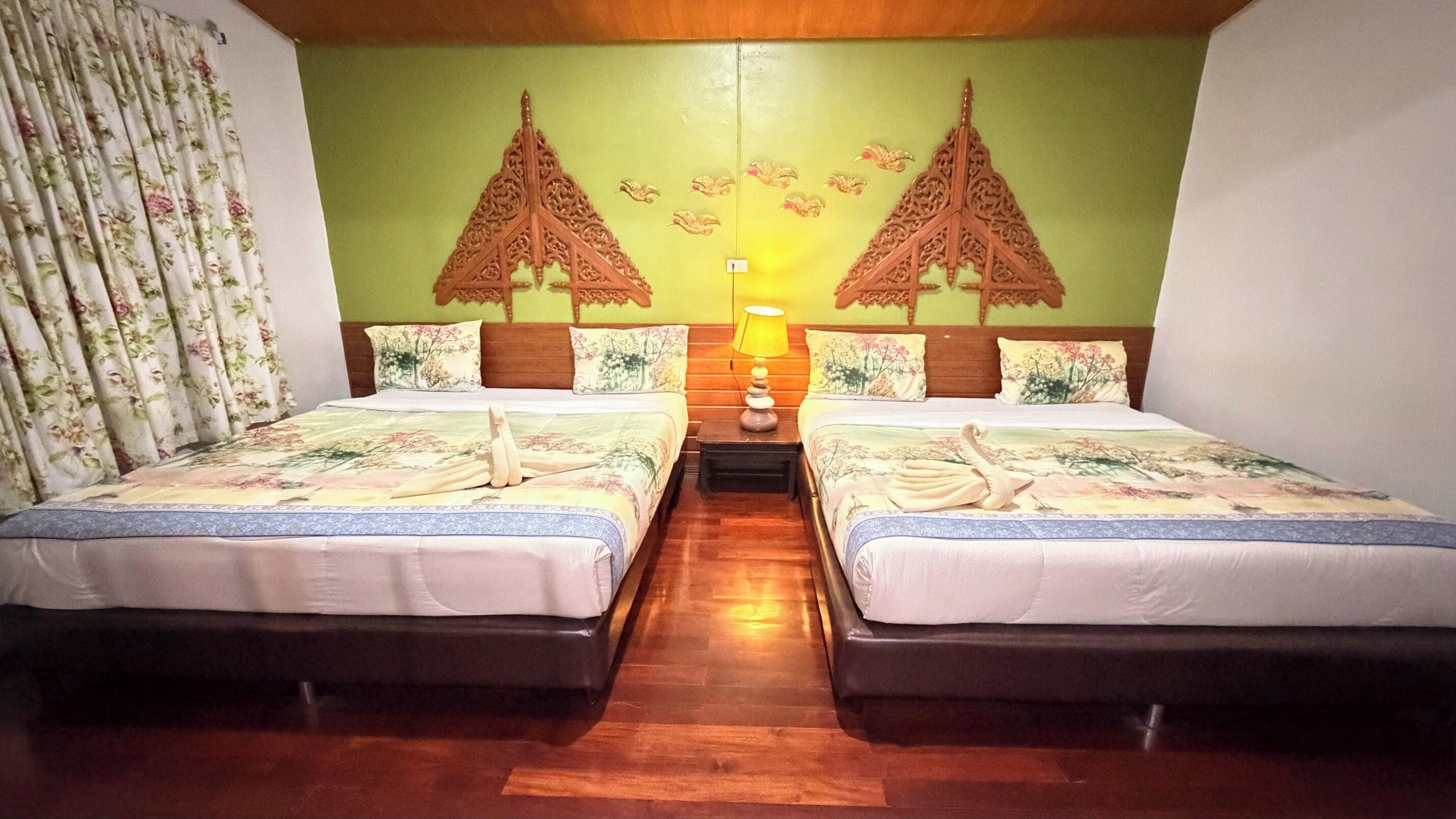 A hotel room with two beds, a wooden headboard, a nightstand with a lamp, and a mural of traditional buildings.