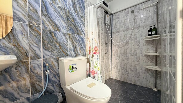 Ein Badezimmer mit Marmorfliesen, einer Toilette, einer Duschkabine mit Glastür und einem Ablagebereich für Toilettenartikel.