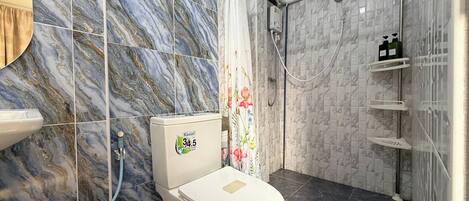 A bathroom with marble tiles, a toilet, a shower with a glass door, and a shelf with toiletries.