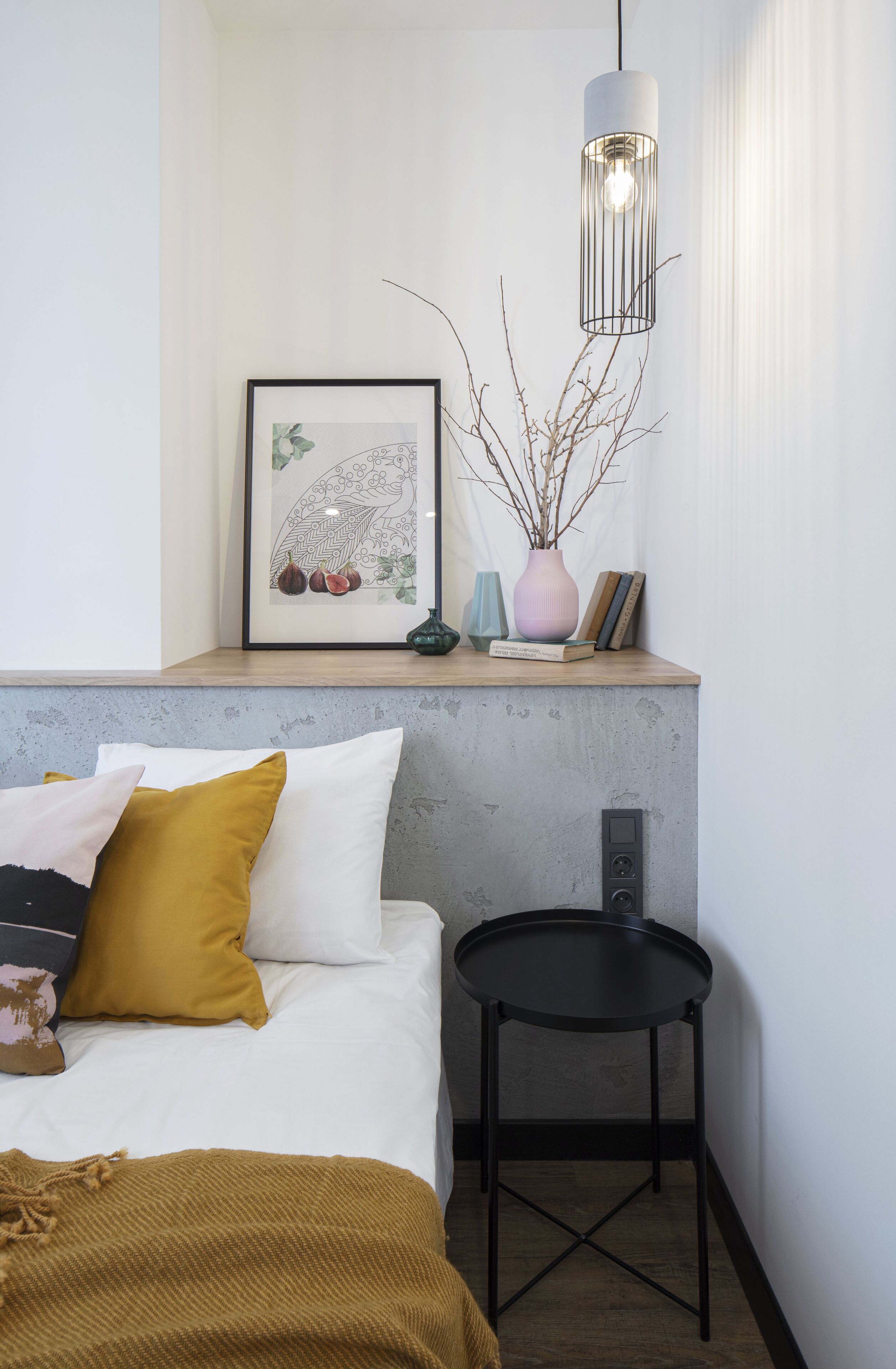 Une chambre à coucher comprenant un lit, une table de chevet, une petite table ronde, un tableau encadré et un luminaire suspendu.