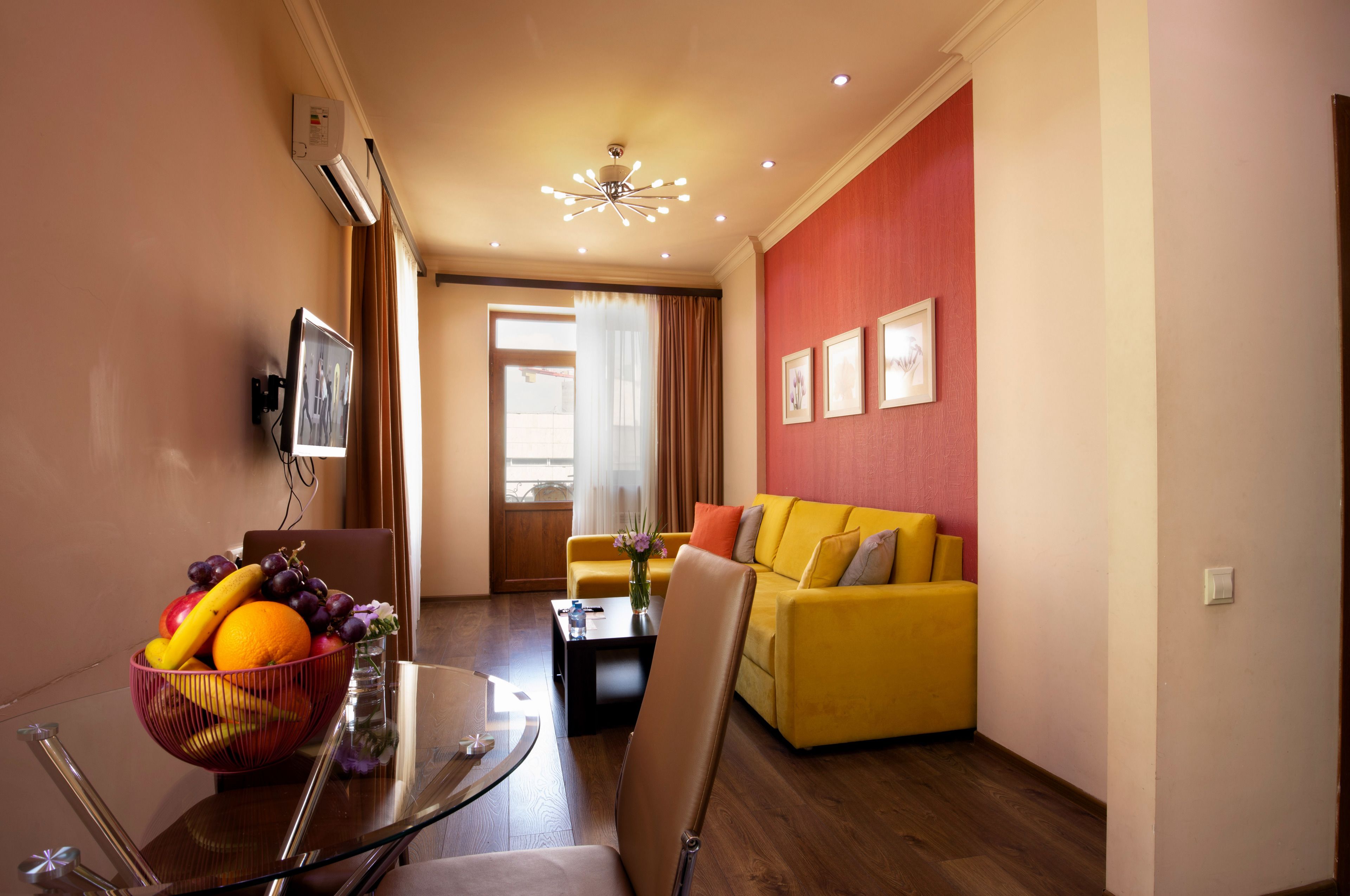 A modern living room with a yellow sofa, a glass coffee table, and a fruit bowl.