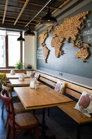 Een café met houten tafels en banken, een wereldkaart gemaakt van houten blokken aan de muur, en hangende pendelverlichting.