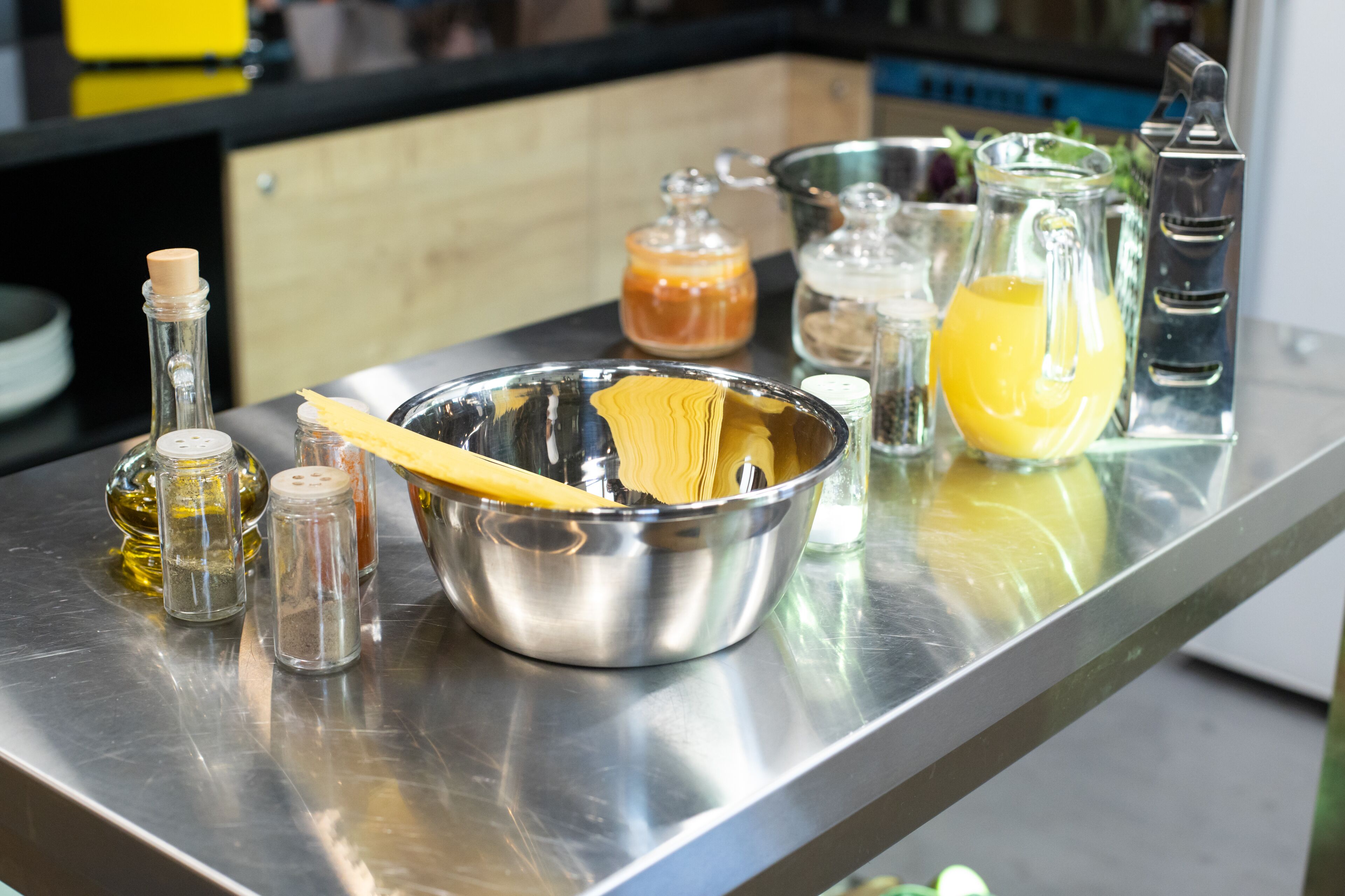 A stainless steel kitchen counter with various cooking utensils, a bowl of pasta, and several glass containers.