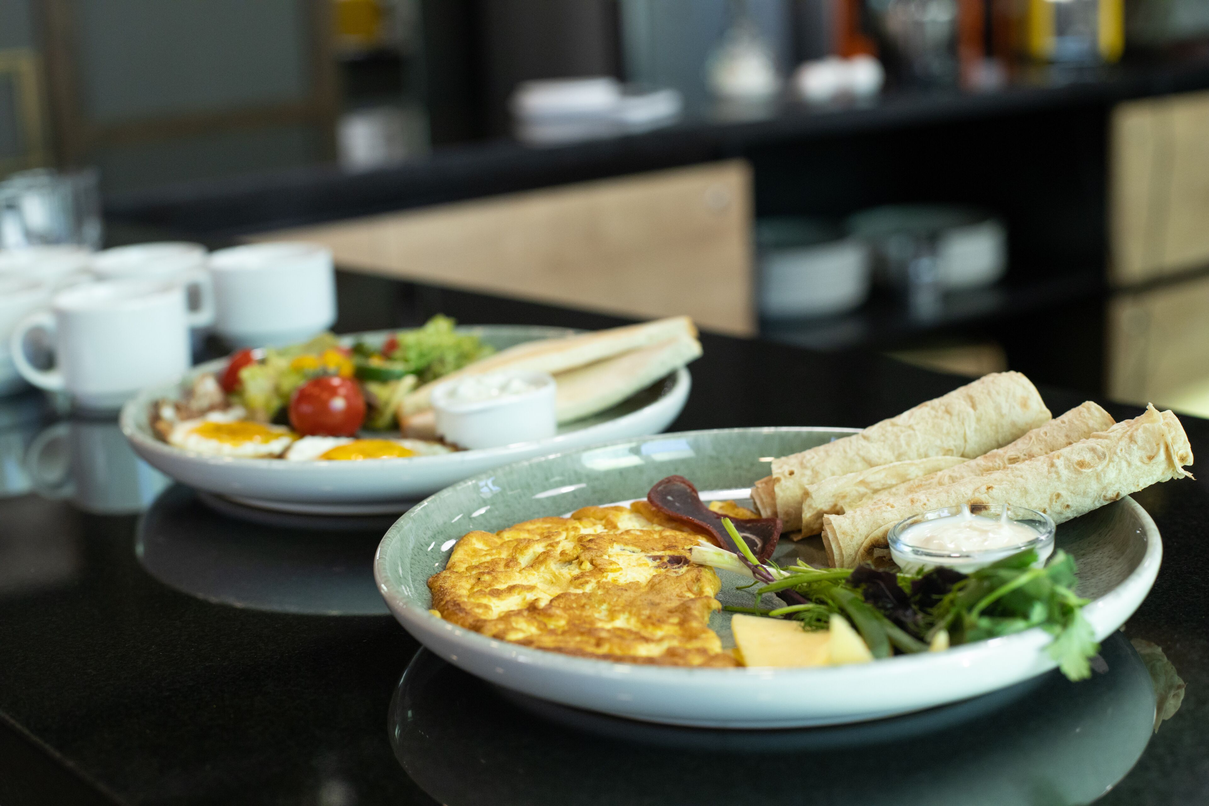 A dining table with plates of food, including an omelette, salad, and wraps.
