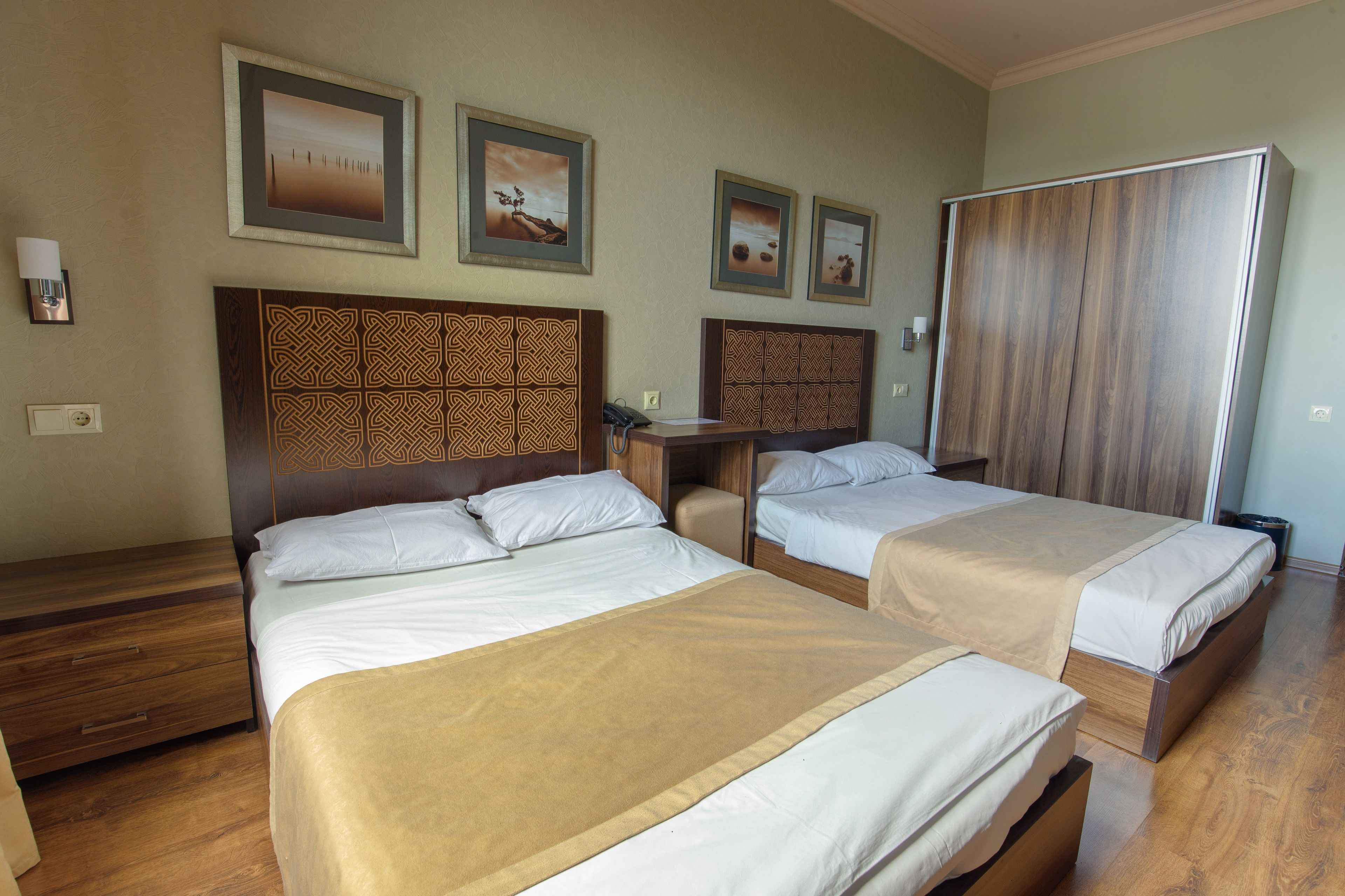 A hotel room with two beds, a wooden headboard, a desk, and a wardrobe.