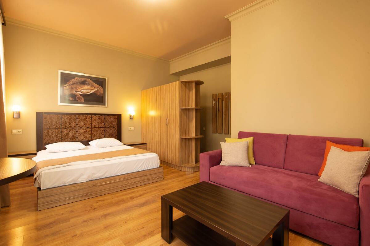 A bedroom with a bed, a wooden wardrobe, a purple sofa, and a wooden coffee table.